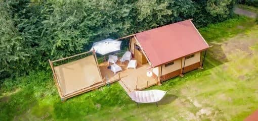 Luchtfoto van de Cozy Lodge met rood dak en veranda, de Teeny Lodge ernaast en een hangmat op het gras
