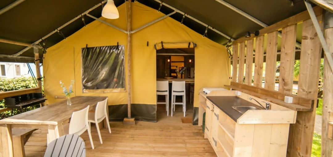 Overdekte veranda van de Safari Lodge met houten eettafel, witte stoelen, buitenkeuken met spoelbak en barbecue
