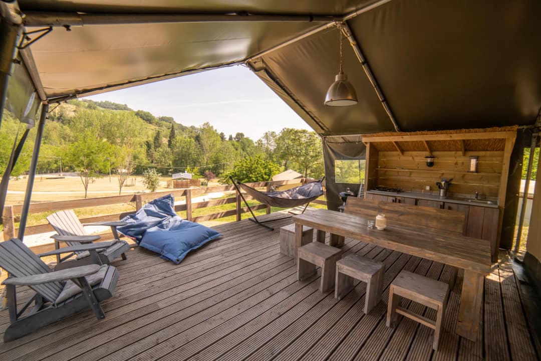 Veranda van de Safari Lodge voor 2 tot 6 personen met tuinstoelen, blauwe zitzakken, hangmat en lange tafel met krukjes boven een grasveld