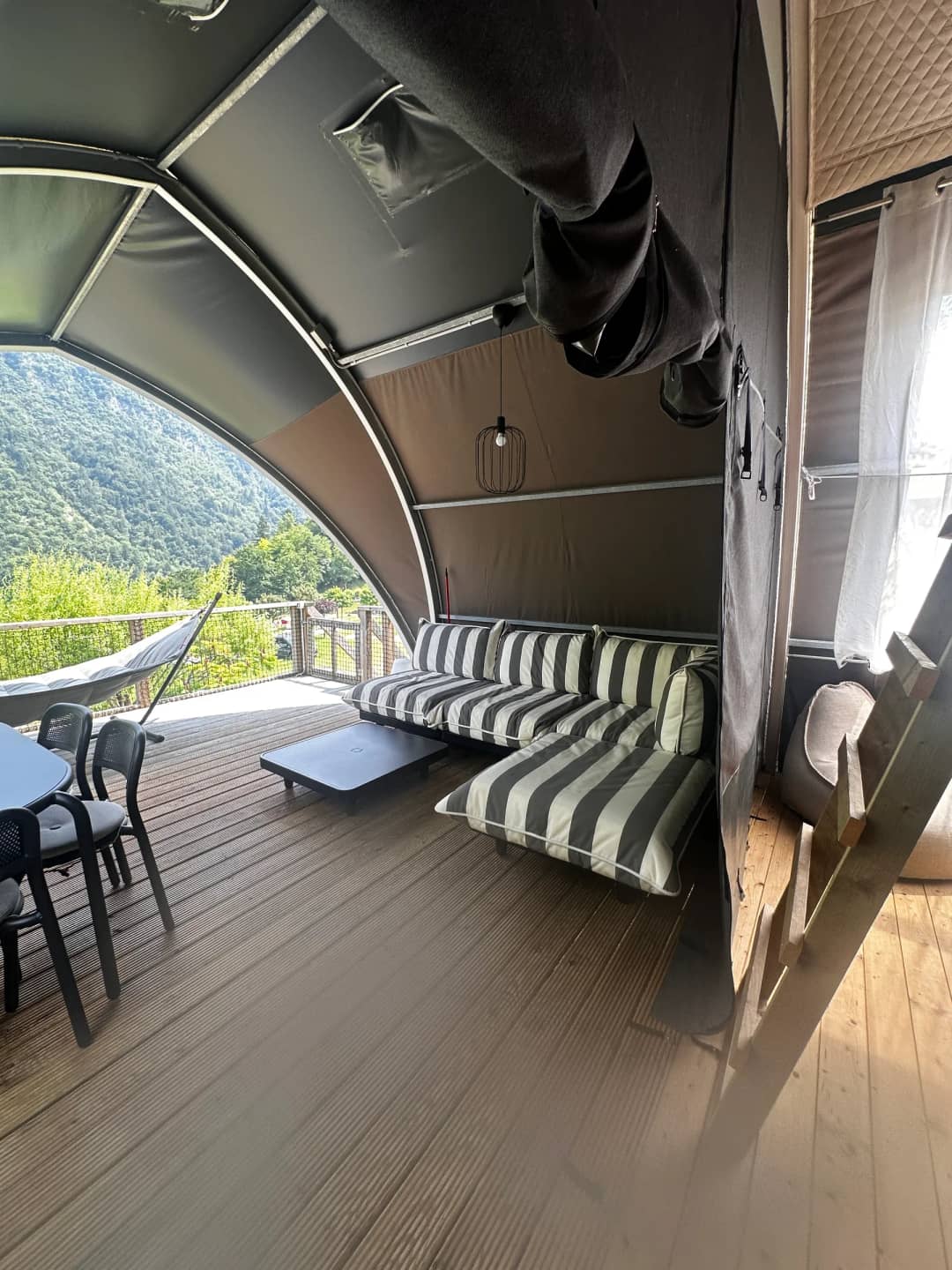Overdekte veranda van de Big Oak Lodge XL met gestreepte loungebank, salontafel en eettafel, met zicht op de bergen
