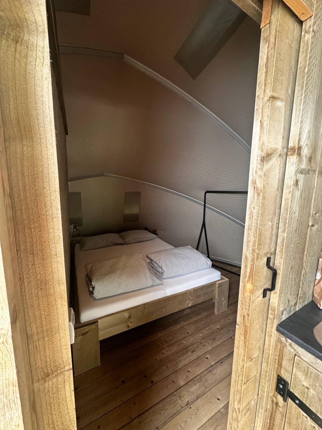 Slaapkamer van de Big Oak Lodge XL met houten tweepersoonsbed onder de gebogen wand, gezien door de deuropening