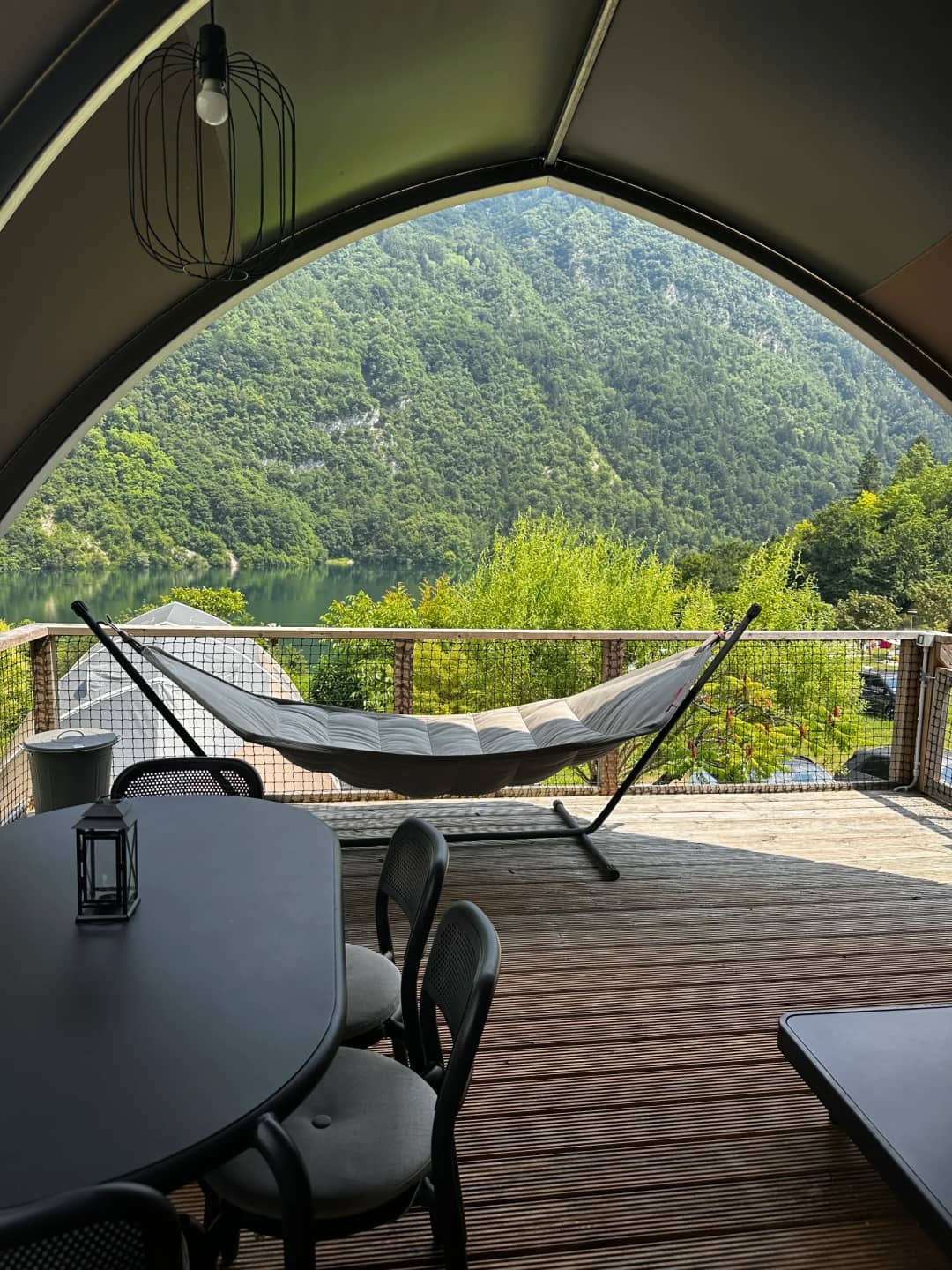 Hangmat en eettafel met lantaarn op de veranda van de Big Oak Lodge XL, met uitzicht op het meer en de bergen