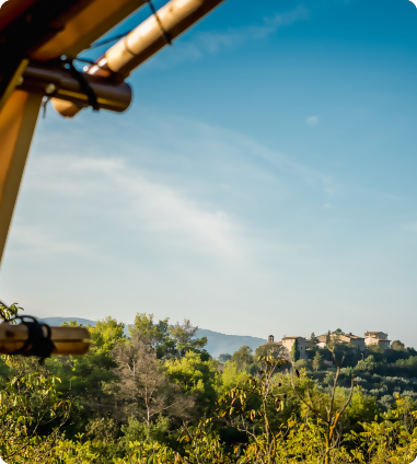 Uitzicht vanaf een lodgetent over de groene heuvels en een idyllisch Italiaans dorpje. Een rustige ochtend met helder licht en een warme glamping-sfeer, zoals je die ervaart op onze locaties in Italië.
